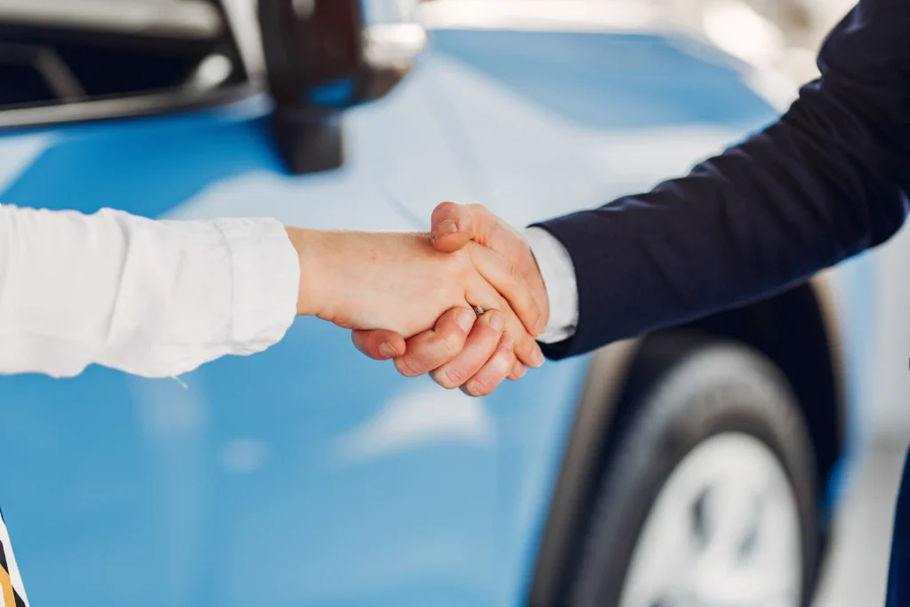 Un couple souriant reçoit les clés de sa nouvelle voiture blanche.